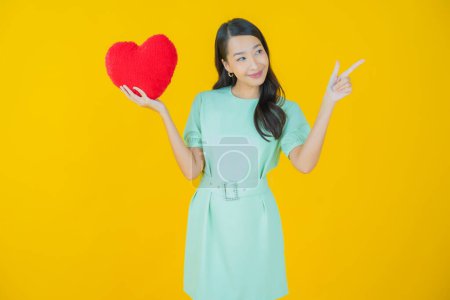 Foto de Retrato hermosa joven asiática mujer sonrisa con corazón almohada forma en color fondo - Imagen libre de derechos