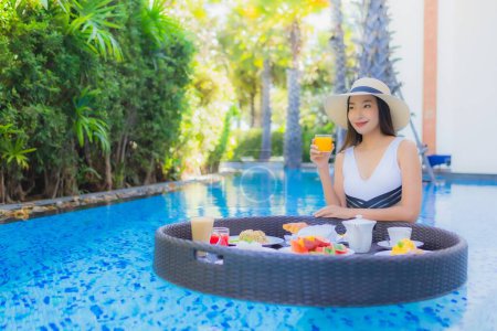 Téléchargez les photos : Portrait belle jeune femme asiatique sourire heureux avec petit déjeuner flottant dans le plateau sur la piscine - en image libre de droit