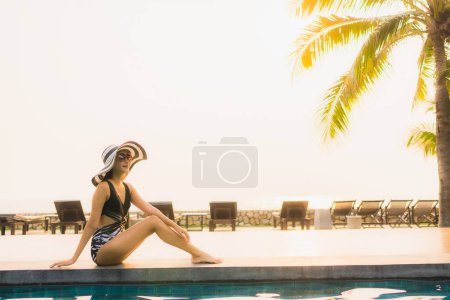 Téléchargez les photos : Portrait belle jeune femme asiatique se détendre autour de la piscine extérieure dans la station hôtelière avec palmier au coucher du soleil ou au lever du soleil pour des vacances de loisirs - en image libre de droit