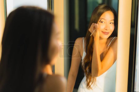 Téléchargez les photos : Portrait belle jeune femme asiatique maquillage avec de la poudre cosmétique et rouge à lèvres sur son visage facial dans la salle de bain intérieure - en image libre de droit