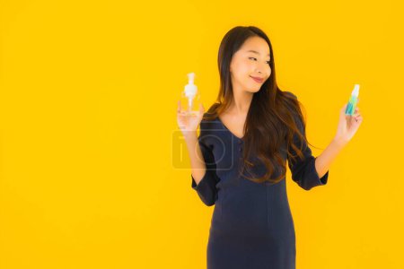Téléchargez les photos : Portrait belle jeune femme asiatique avec gel d'alcool et spray pour protéger du coronavirus ou covid19 sur fond jaune isolé - en image libre de droit