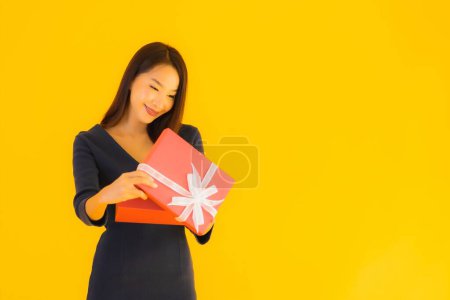 Téléchargez les photos : Portrait belle jeune femme asiatique avec boîte cadeau sur fond jaune isolé - en image libre de droit