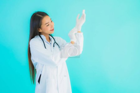Téléchargez les photos : Portrait beau jeune médecin asiatique avec gant pour une utilisation en clinique ou à l'hôpital sur fond bleu isolé - en image libre de droit