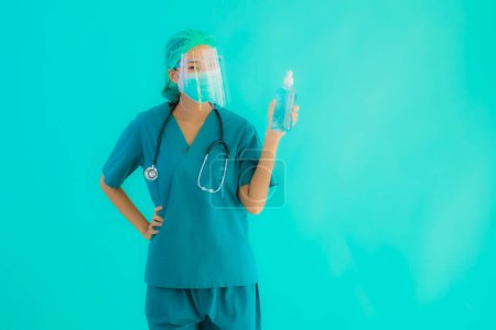 Téléchargez les photos : Portrait belle jeune asiatique médecin femme avec gel d'alcool pour protéger contre le coronavirus ou covid19 sur fond bleu isolé - en image libre de droit