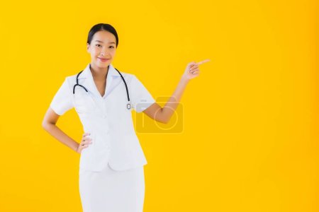 Téléchargez les photos : Portrait belle jeune femme asiatique thai infirmière sourire heureux prêt pour le travail pour le patient à la clinique ou à l'hôpital sur fond jaune isolé - en image libre de droit