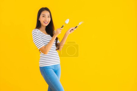 Foto de Retrato hermosa joven asiática mujer mostrar cuchara y tenedor listo para comer en amarillo aislado fondo - Imagen libre de derechos