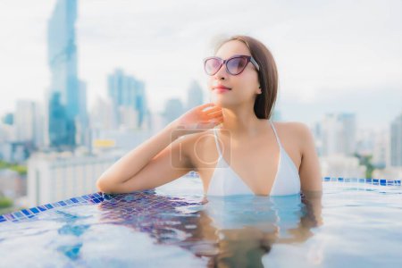 Foto de Retrato hermosa joven mujer asiática relajarse feliz sonrisa ocio alrededor de piscina al aire libre con paisaje urbano - Imagen libre de derechos