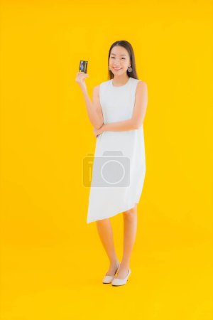 Téléchargez les photos : Portrait belle jeune femme asiatique avec carte de crédit pour les achats en ligne sur fond jaune isolé - en image libre de droit