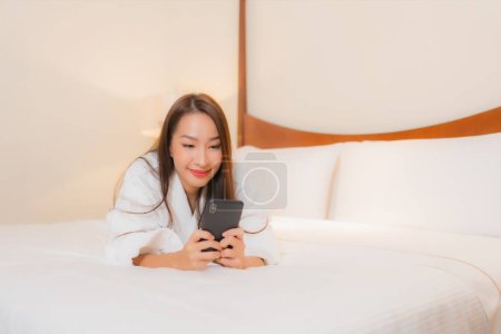 Photo for Portrait beautiful young asian woman use smart mobile phone on bed in bedroom interior - Royalty Free Image