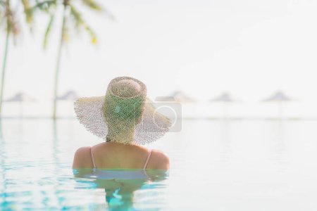 Foto de Retrato hermosa mujer asiática joven relajarse ocio alrededor de la piscina al aire libre con vista al mar playa océano en viajes de vacaciones - Imagen libre de derechos