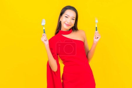 Foto de Retrato hermosa joven asiática mujer con cuchara y tenedor listo para comer sobre fondo amarillo - Imagen libre de derechos