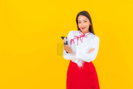 Téléchargez les photos : Portrait belle jeune femme asiatique avec maquillage pinceau cosmétique sur fond jaune - en image libre de droit