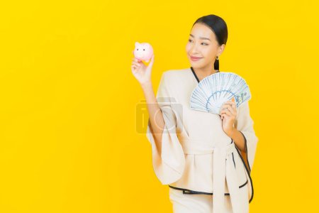 Photo for Portrait beautiful young business asian woman with a lot of cash money and piggy bank on yellow background - Royalty Free Image