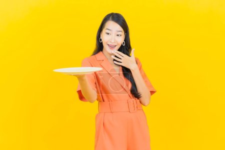 Foto de Retrato hermosa joven mujer asiática sonrisa con plato vacío sobre fondo de color amarillo - Imagen libre de derechos