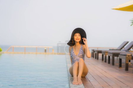 Téléchargez les photos : Portrait jeune femme asiatique sourire heureux se détendre autour de la piscine extérieure dans la station hôtelière pour des vacances de voyage - en image libre de droit