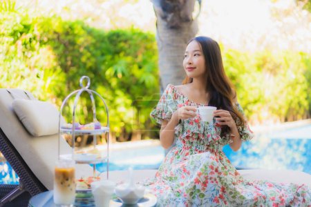 Téléchargez les photos : Beau portrait jeune femme asiatique avec ensemble de thé après-midi avec café assis sur la chaise autour de la piscine dans la station hôtelière - en image libre de droit