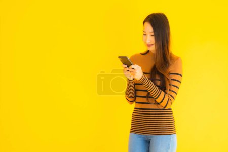 Photo for Beautiful young asian woman use smart mobile phone or cellphone with many action on yellow isolated background - Royalty Free Image