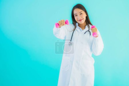 Téléchargez les photos : Portrait belle jeune asiatique médecin femme avec haltère rose pour l'exercice sur fond bleu isolé - en image libre de droit