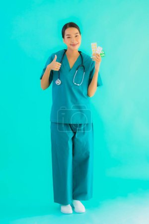 Téléchargez les photos : Portrait belle jeune asiatique médecin femme avec pilule ou médicament et médecine sur fond bleu isolé - en image libre de droit