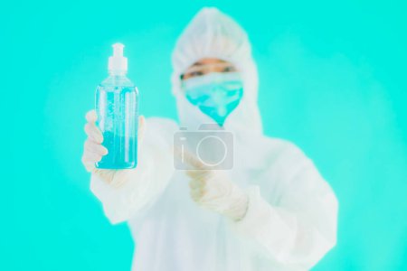 Photo for Portrait beautiful young asian doctor woman wear ppe suite and mask with alcohol gel on blue isolated background - Royalty Free Image