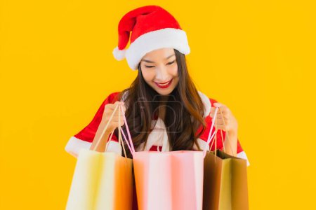 Photo for Portrait beautiful young asian woman wear christmas clothes hat with a lot of shopping bag on yellow isolated background - Royalty Free Image