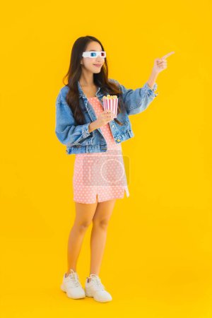 Téléchargez les photos : Portrait belle jeune femme asiatique profiter heureux avec téléphone pop-corn et regarder le film sur fond jaune isolé - en image libre de droit