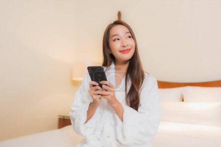 Foto de Retrato hermosa joven mujer asiática uso inteligente teléfono móvil en la cama en el interior del dormitorio - Imagen libre de derechos