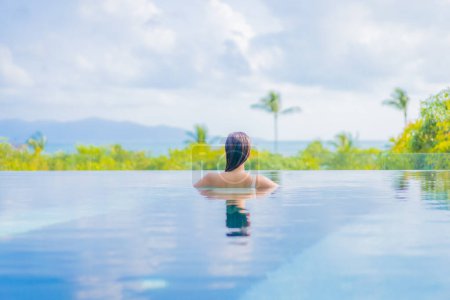Téléchargez les photos : Portrait belle jeune femme asiatique profiter autour de la piscine extérieure avec vue sur l'océan de mer en voyage vacances - en image libre de droit