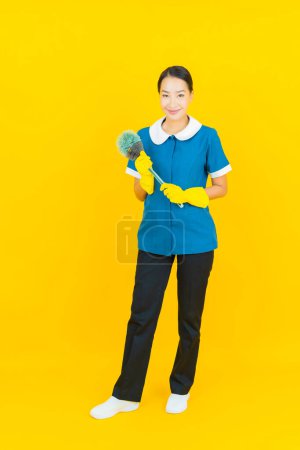 Foto de Retrato hermosa joven asiática mujer mucama y limpieza sonrisa con acción en color amarillo fondo - Imagen libre de derechos