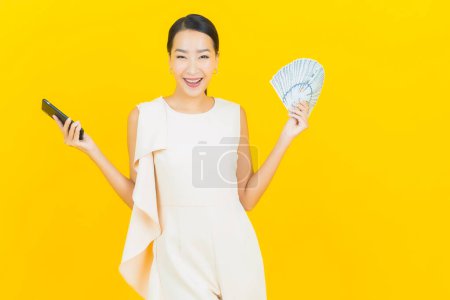 Foto de Retrato hermosa joven asiática mujer sonrisa con un montón de dinero en efectivo y dinero en color amarillo fondo - Imagen libre de derechos