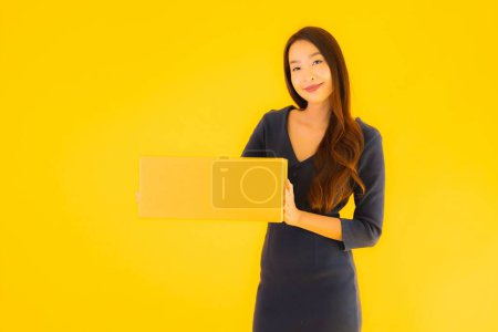 Téléchargez les photos : Portrait belle jeune femme asiatique avec boîte en carton packkage prêt pour l'expédition sur fond jaune isolé - en image libre de droit