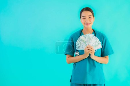 Photo for Portrait beautiful young asian doctor woman show money and cash on blue isolated background - Royalty Free Image