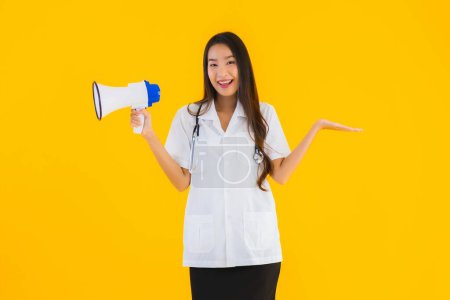 Foto de Retrato hermosa joven asiática médico mujer uso megáfono en amarillo aislado fondo - Imagen libre de derechos