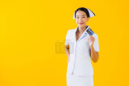 Foto de Retrato hermosa joven asiática mujer tailandesa enfermera con tarjeta de crédito en amarillo aislado fondo - Imagen libre de derechos