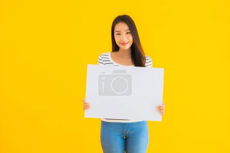 Téléchargez les photos : Portrait belle jeune femme asiatique montrer vide panneau d'affichage blanc signe sur fond jaune isolé - en image libre de droit