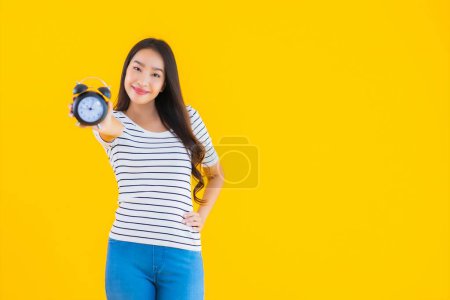 Foto de Retrato hermosa joven asiática mujer mostrar reloj o alarma en amarillo aislado fondo - Imagen libre de derechos