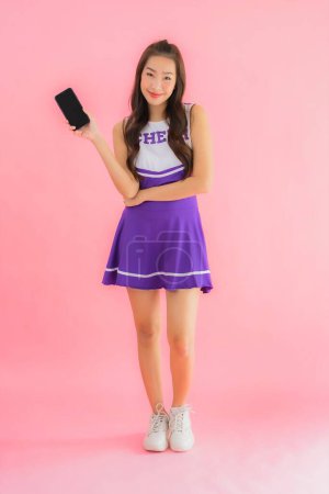 Téléchargez les photos : Portrait belle jeune asiatique femme pom-pom girl utiliser téléphone mobile intelligent sur fond rose isolé - en image libre de droit