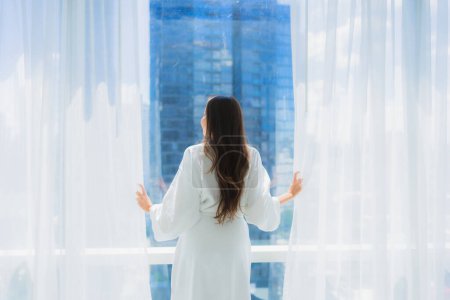 Foto de Retrato hermosa joven asiática mujer ventana de cortina abierta y mirar fuera de la ventana para la vista - Imagen libre de derechos