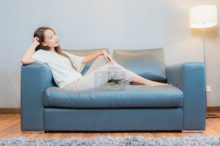 Téléchargez les photos : Portrait belle jeune femme asiatique se détendre sur canapé dans le salon intérieur - en image libre de droit