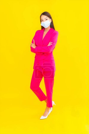 Téléchargez les photos : Portrait belle jeune femme asiatique porter un masque pour protéger coronavirus ou covid19 sur fond de couleur jaune - en image libre de droit