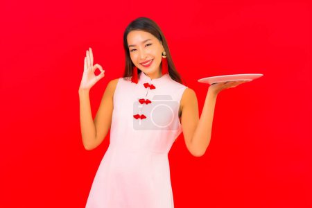 Foto de Retrato hermosa joven asiática mujer con plato vacío en rojo aislado fondo - Imagen libre de derechos