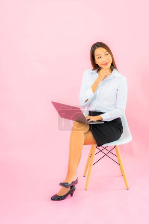 Téléchargez les photos : Portrait belle jeune femme asiatique avec ordinateur portable sur fond de couleur rose - en image libre de droit