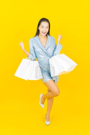Foto de Retrato hermosa joven mujer asiática sonrisa con bolsa de compras en color amarillo fondo - Imagen libre de derechos