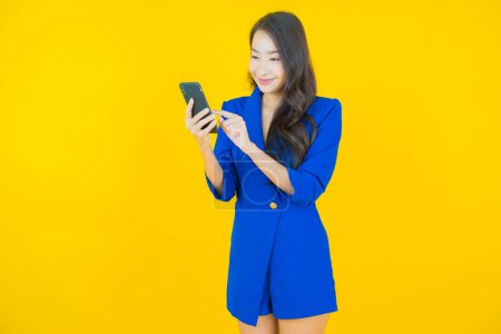 Téléchargez les photos : Portrait belle jeune femme asiatique sourire avec téléphone portable intelligent sur fond de couleur - en image libre de droit