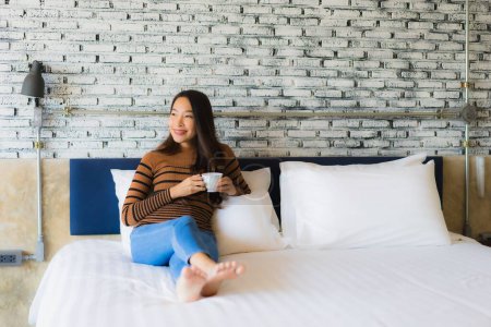 Foto de Joven mujer asiática con taza de café en la cama en el interior del dormitorio - Imagen libre de derechos