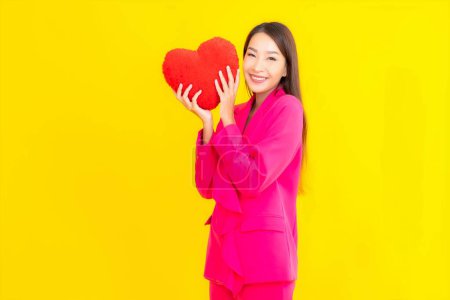 Foto de Retrato hermosa joven asiática mujer con corazón almohada forma en amarillo aislado fondo - Imagen libre de derechos