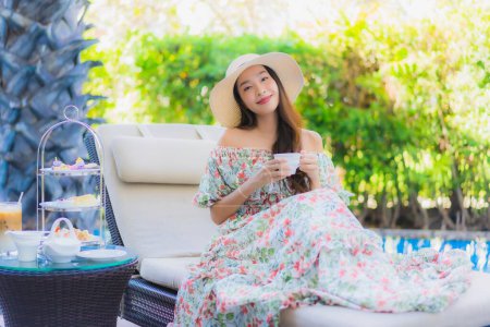Photo for Beautiful portrait young asian woman with afternnoon tea set with coffee sit on chair around swimming pool in hotel resort - Royalty Free Image