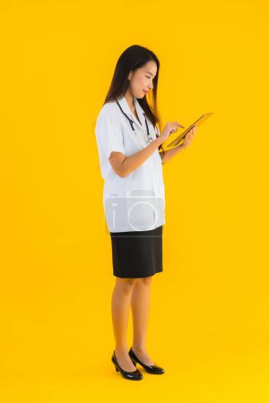 Foto de Retrato hermosa joven asiático médico mujer uso inteligente tableta dispositivo en amarillo aislado fondo - Imagen libre de derechos