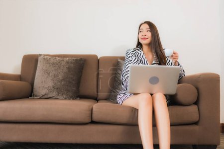 Foto de Retrato hermosa joven mujer asiática uso ordenador portátil en el sofá en la sala de estar área interior - Imagen libre de derechos