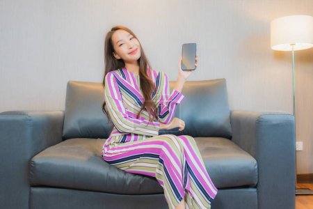 Téléchargez les photos : Portrait belle jeune femme asiatique utiliser téléphone portable intelligent sur canapé dans le salon intérieur - en image libre de droit